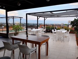 An outdoor patio with tables and chairs, a view of the cityscape, and potted plants.