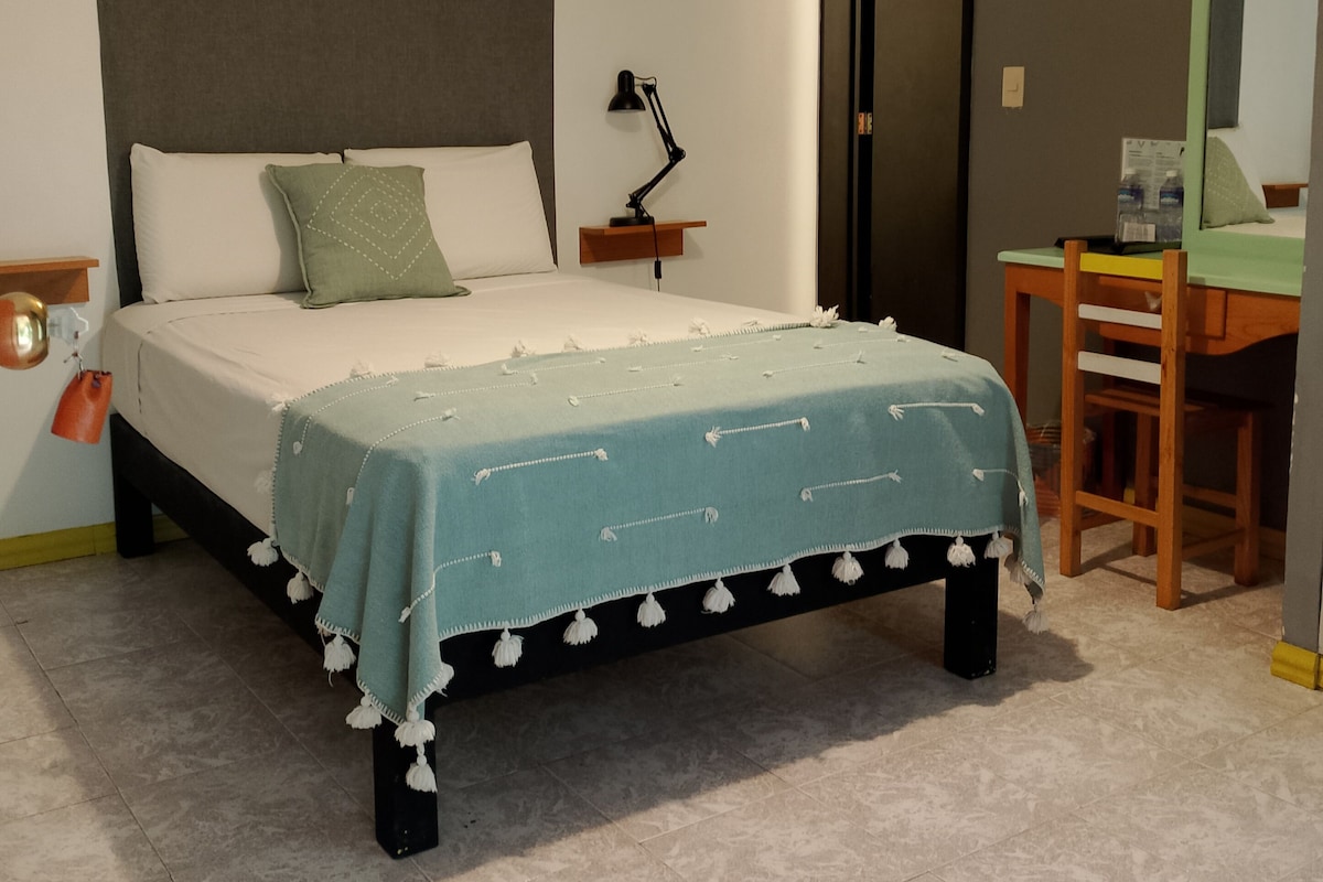 Een slaapkamer met een bed, nachtkastje, lamp, stoel en een bureau met spiegel.