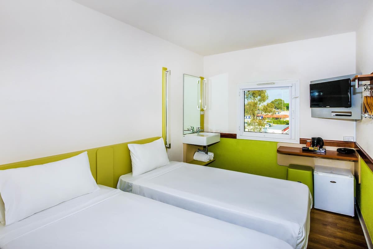 A room with two beds, a sink, a mirror, a television, and a window.