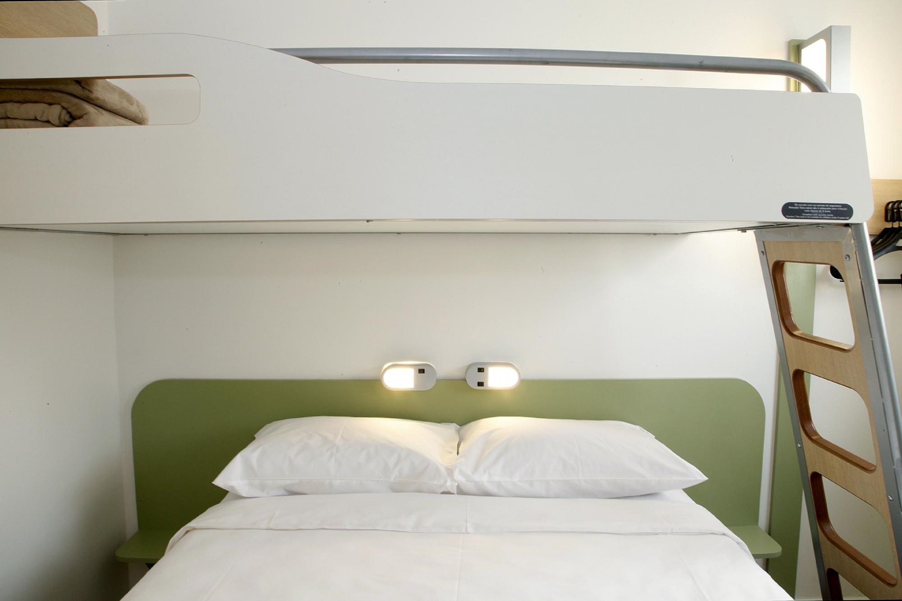 Un letto a castello con un poggiatesta verde, due lampade da comodino e una scala.