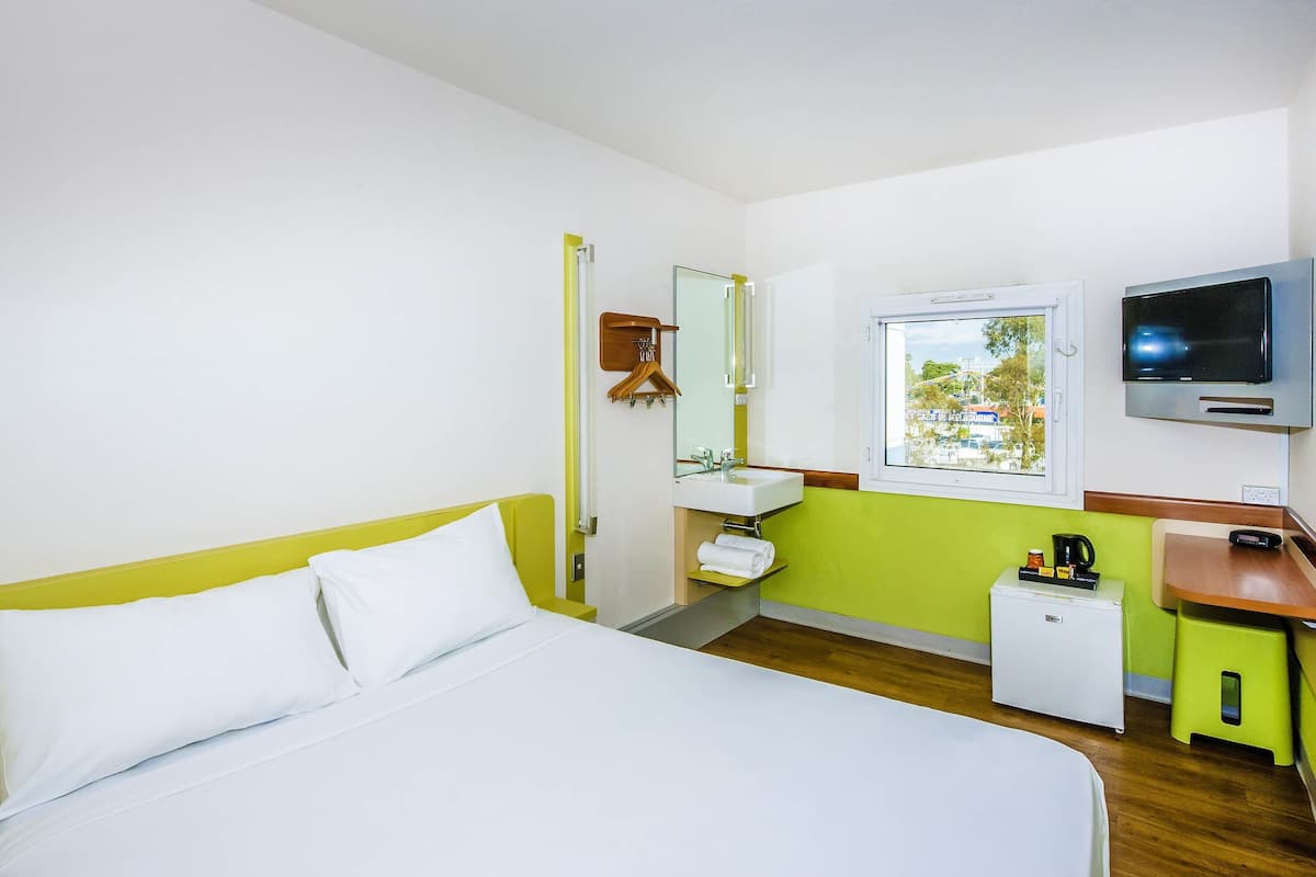 A hotel room with a bed, a TV, a sink, and a window.