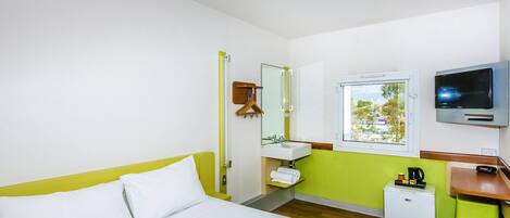 Una habitación de hotel con una cama, televisor, lavamanos y ventana.