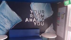 A room with a blue sofa, two small round tables, and a wall with a message saying "YOUR ROOM ALWAYS YOU". - ibis Budget Dandenong (Dandenong)