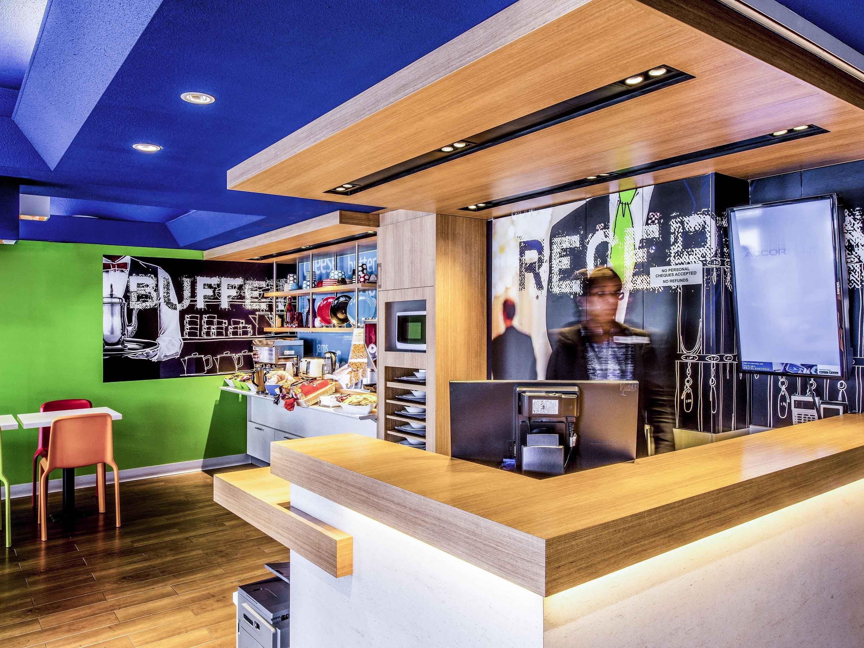 A modern reception area with a wooden counter, a green wall, and a coffee station.