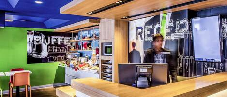 A modern reception area with a wooden counter, a green wall, and a coffee station.