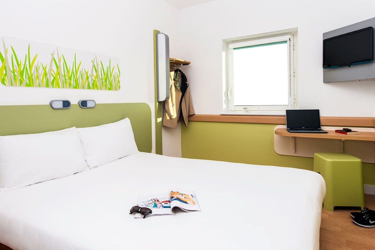 Habitación de hotel con cama, escritorio, computadora portátil, televisor y ventana.