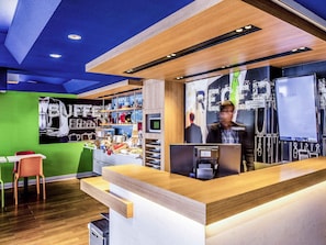 A modern reception area with a wooden counter, a green wall, and a coffee station.