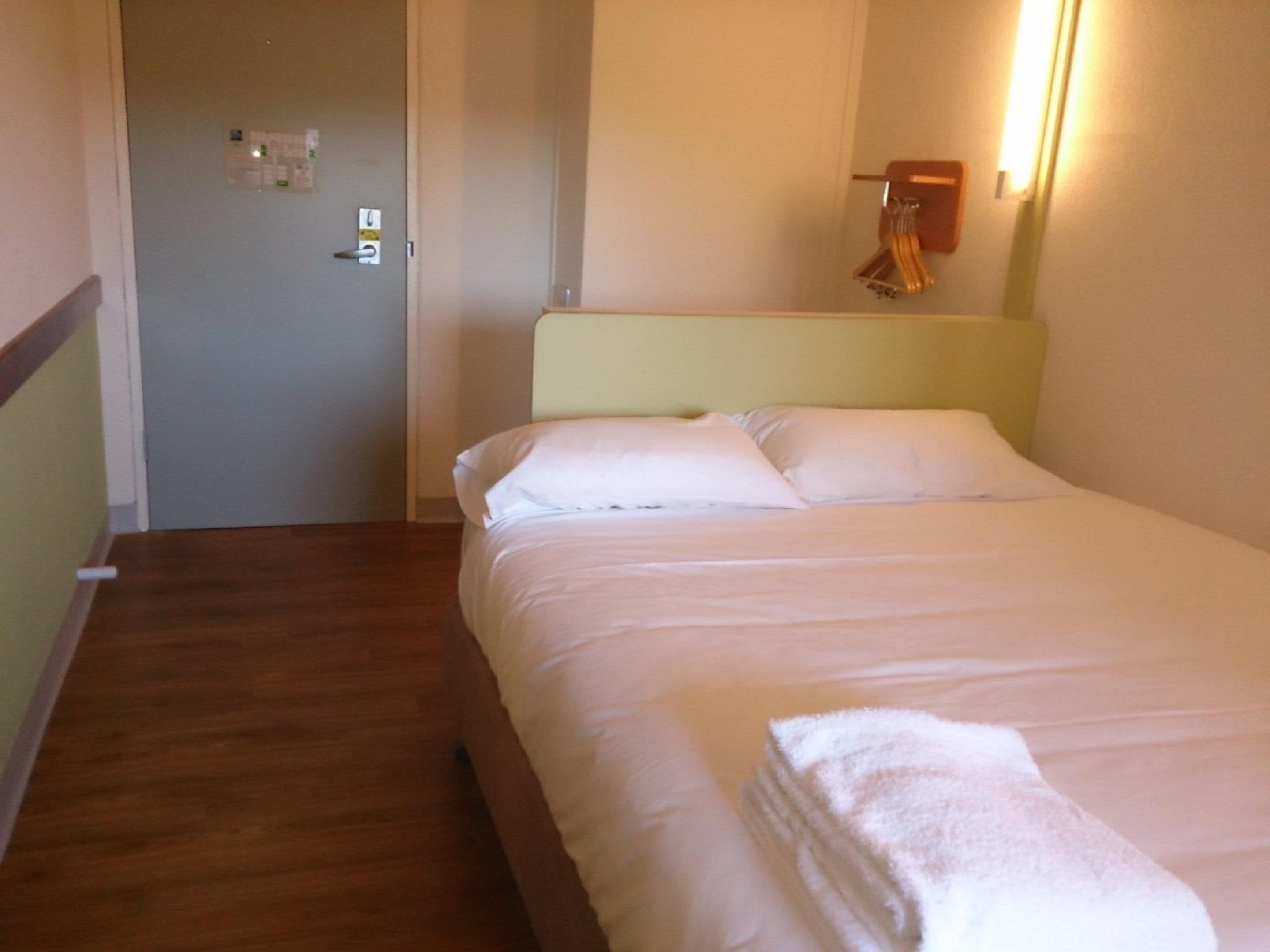 Habitación de hotel con cama, suelo de madera, puerta y aplique.