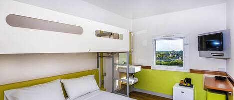 Habitación de hotel con literas, cama individual, televisor, ventana con vista y una pequeña mesa de trabajo con cafetera.