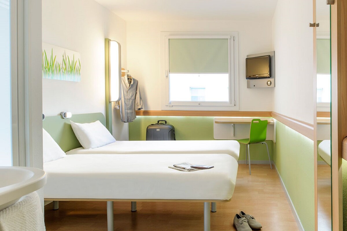 Habitación de hotel con dos camas, un escritorio, una silla, un televisor y una ventana.