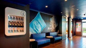 A modern hotel lobby with a reception desk, seating area, and a large wall mural. - ibis Budget Dandenong (Dandenong)