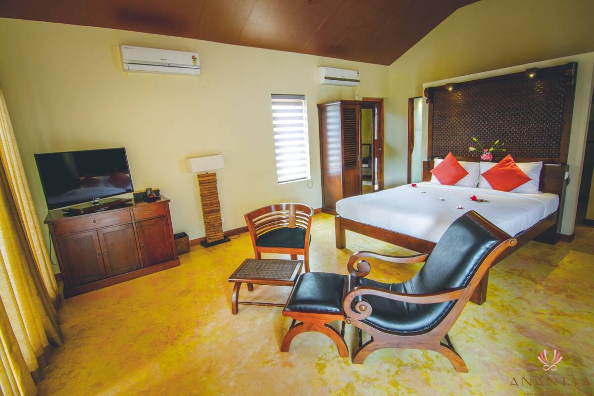 A hotel room with a bed, a television, a desk, two chairs, and a wardrobe.