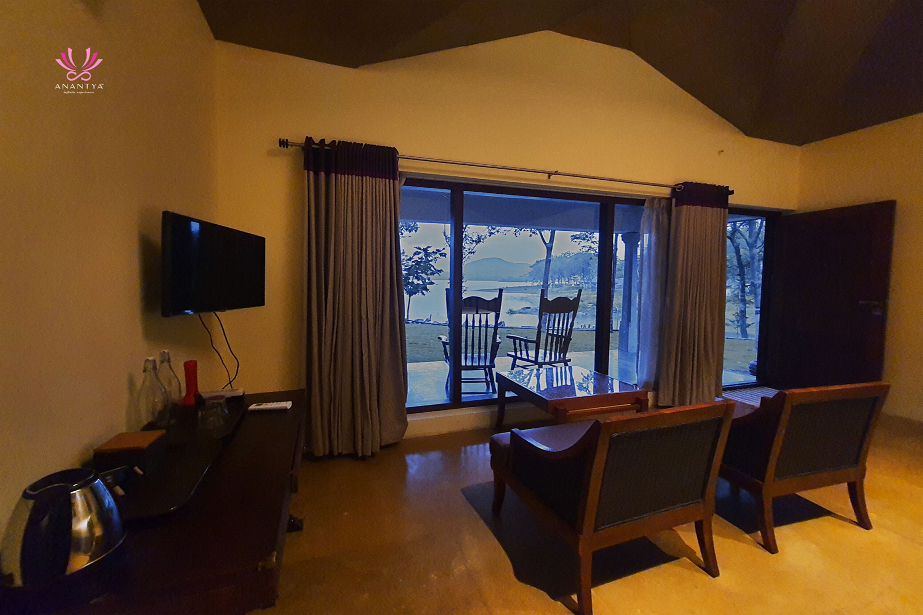 A hotel room with a large window, a flat-screen TV, a desk, and two chairs.