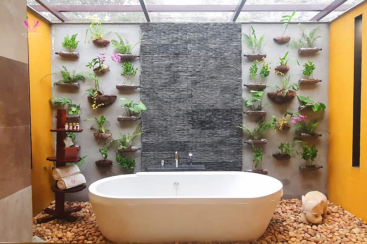A bathroom with a freestanding bathtub, a stone wall, and multiple potted plants arranged on the walls.