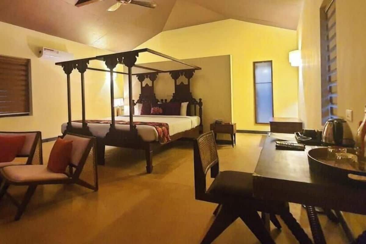 A room with a four-poster bed, a dining table with chairs, a small table with a chair, and a window with blinds.