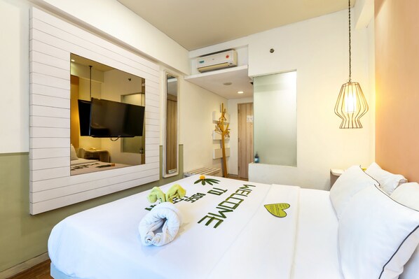 A hotel room with a bed, a TV mounted on the wall, an air conditioning unit, and a hanging light fixture.