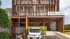 A modern hotel with a prominent sign, multiple balconies, and a white car parked in front. - Boss Legian Hotel Powered by Archipelago (Legian)
