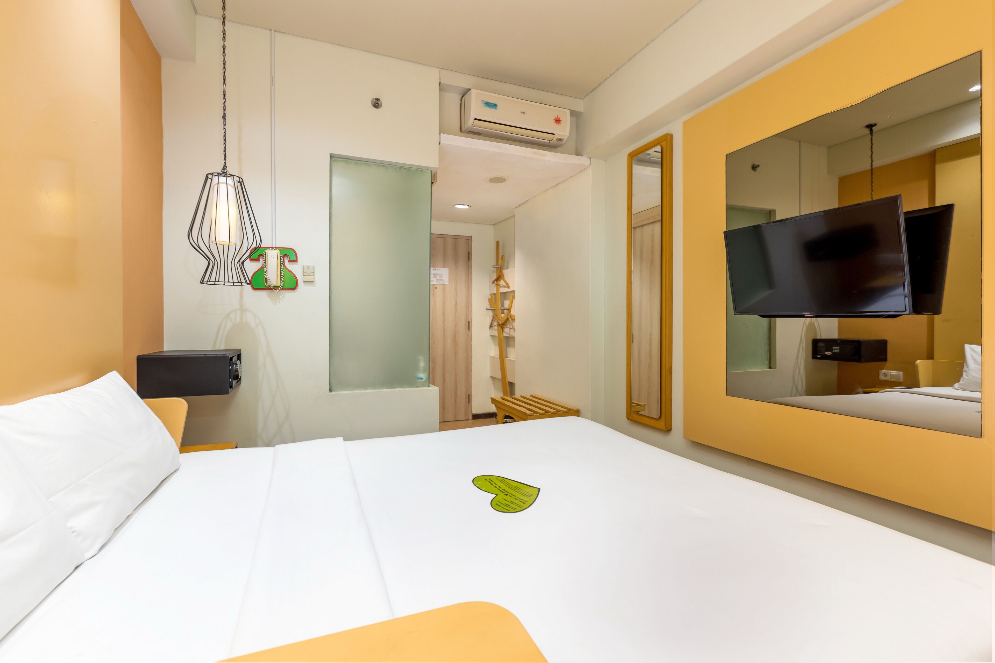 Ett hotellrum med en säng, en tv, en spegel och en luftkonditioneringsanläggning.