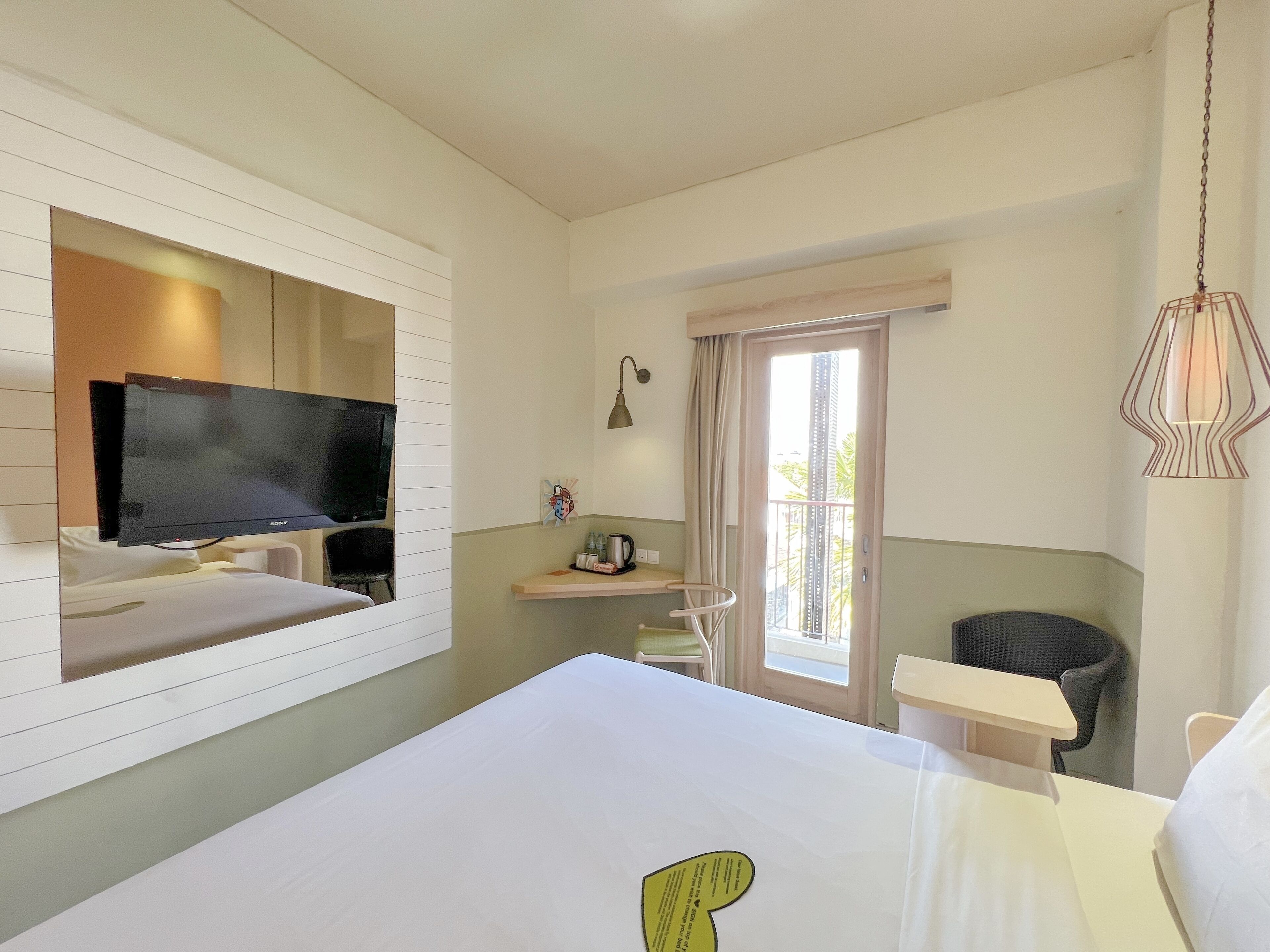 A hotel room with a bed, a TV mounted on the wall, a small table, a chair, and a window with curtains.