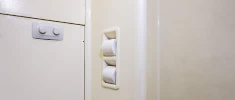A small, white bathroom with a toilet, a shower stall, and a toilet paper holder.