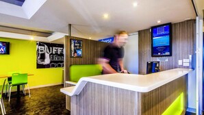 A modern reception area with a counter, green seating, and a TV screen.