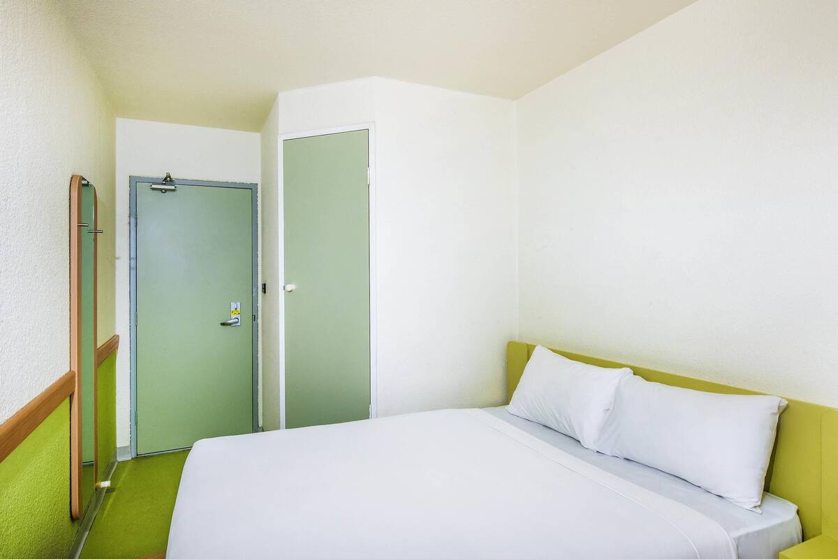 A hotel room with a bed, a green wall, and a door.