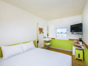 A hotel room with a bed, a sink, a mirror, a television, and a window.