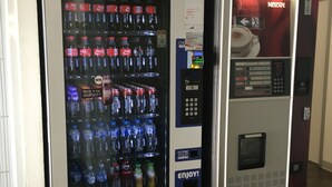 A vending machine with Coca-Cola and other beverages, a Nescafé coffee machine, and a sign for ibis budget hotels.
