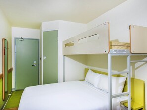 Una cama litera con colchón y almohadas blancas, una puerta verde y una pared blanca.