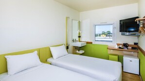 A hotel room with two beds, a small sink, a television, and a window with a view.
