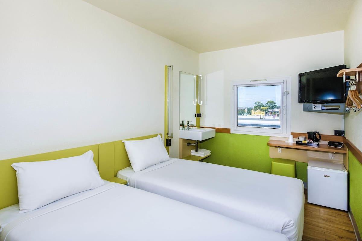 A hotel room with two beds, a small sink, a television, and a window with a view.