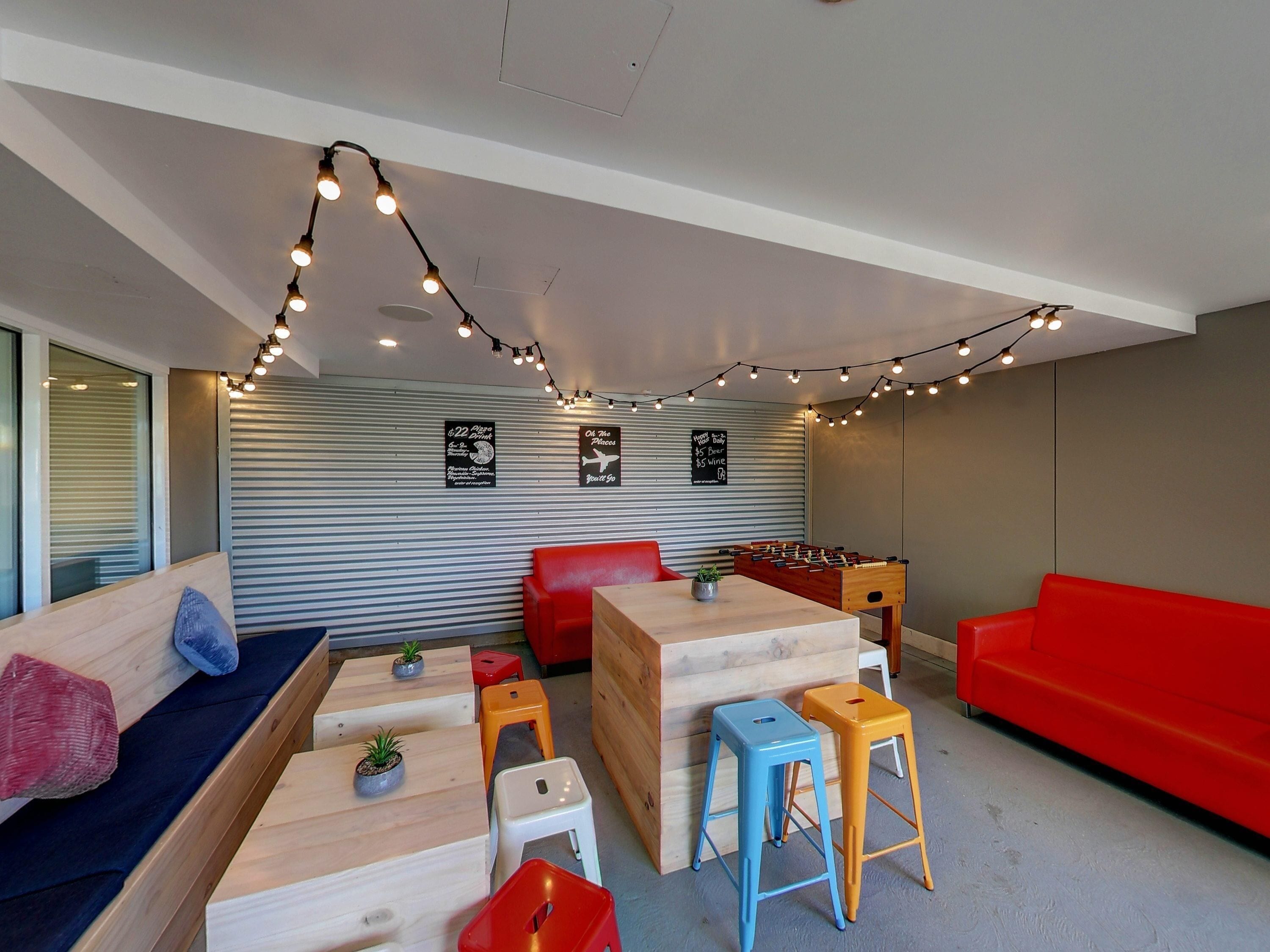 A modern lounge area with a foosball table, red and blue stools, and a foosball table.