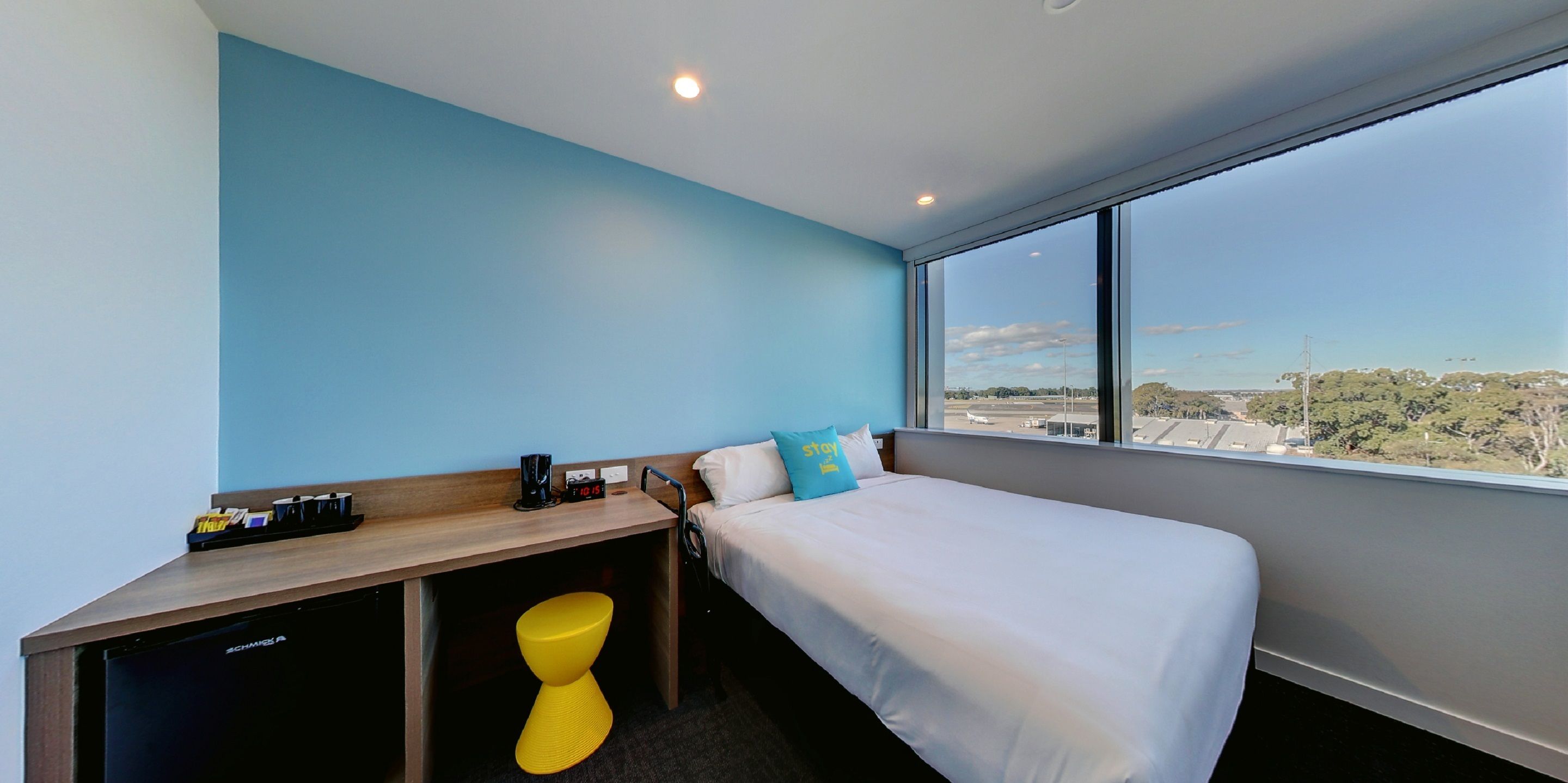 Ein Hotelzimmer mit Bett, Schreibtisch, Stuhl und einem großen Fenster mit Blick auf die Stadt.