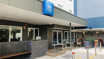 Exterior de um hotel ibis budget com design moderno, incluindo fachada de pedra, uma placa azul e uma rampa que leva à entrada.