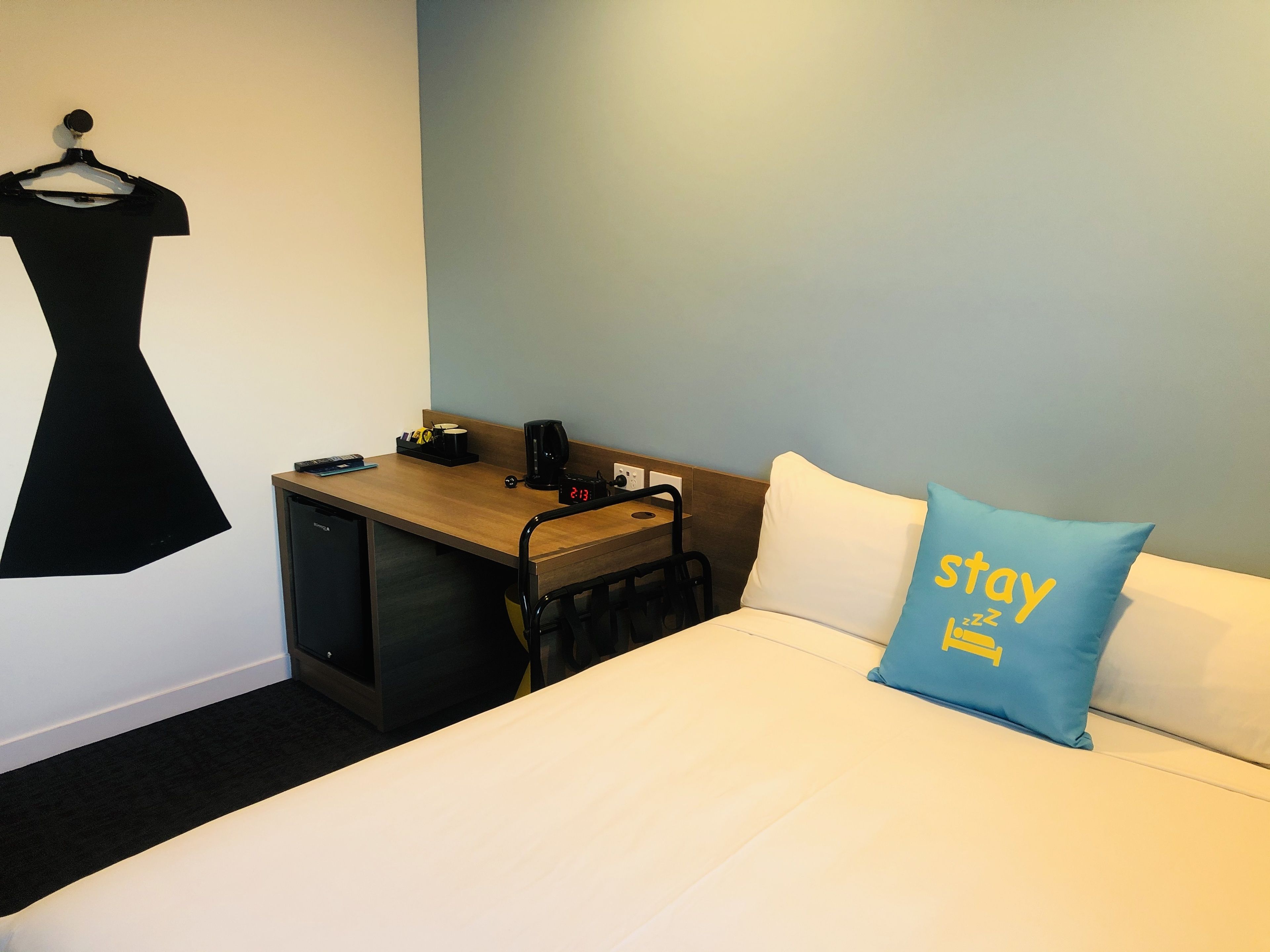 Een hotelkamer met een bed, bureau, koffiezetapparaat, klok en een decoratie aan de muur.
