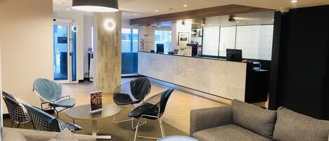 A modern lounge area with a sofa, chairs, a small table, and a reception desk.