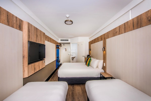 Una habitación de hotel con dos camas, un televisor montado en la pared y una pared de acento de madera.