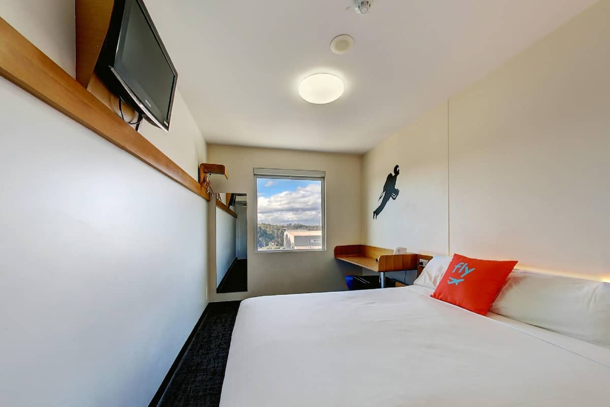 Een hotelkamer met een bed, een bureau, een stoel, een televisie, een raam met uitzicht en een plafondlamp.