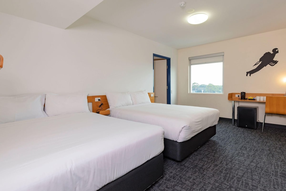 Een hotelkamer met twee enkele bedden, een klein bureau met stoel, een raam met uitzicht en een wanddecoratie in silhouette.