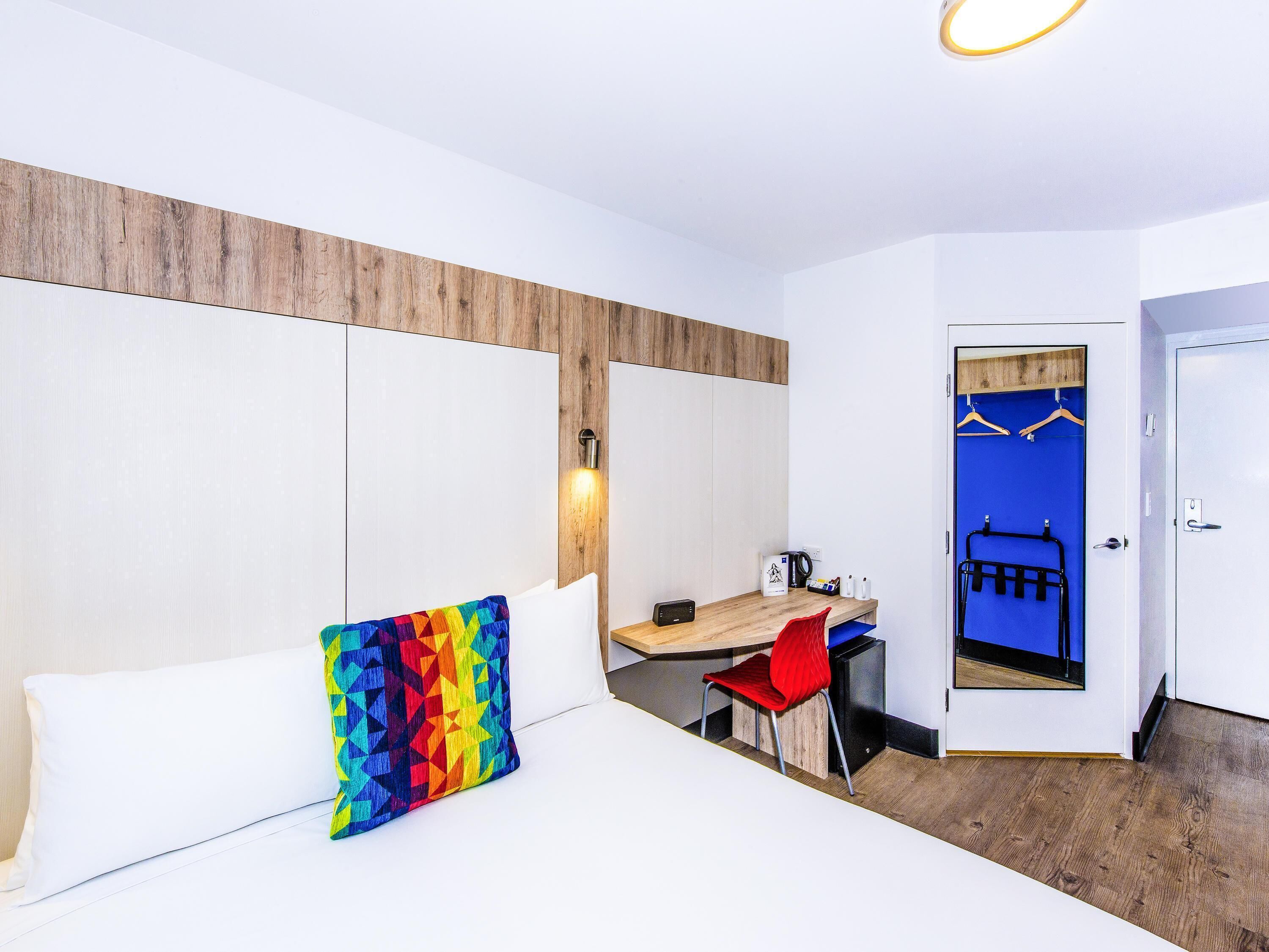 A hotel room with a bed, a desk, a chair, a wardrobe, and a door.