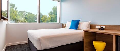 Habitación de hotel con cama, escritorio, silla y ventana con vistas a árboles.