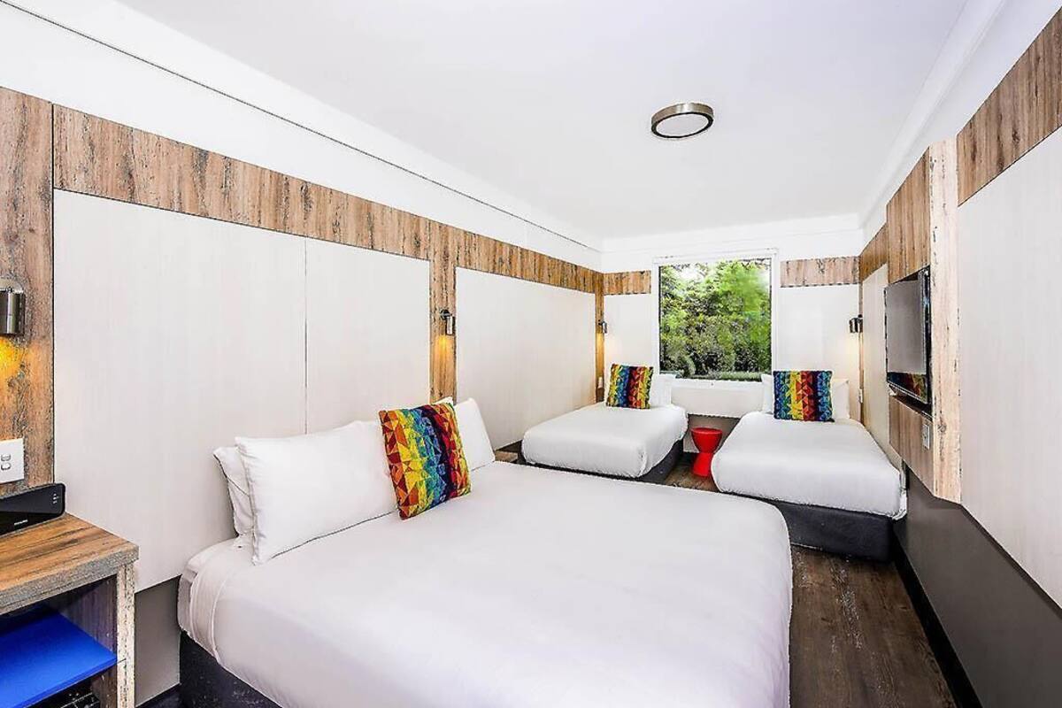 Een hotelkamer met een groot bed, een televisie en een raam met uitzicht op groen.