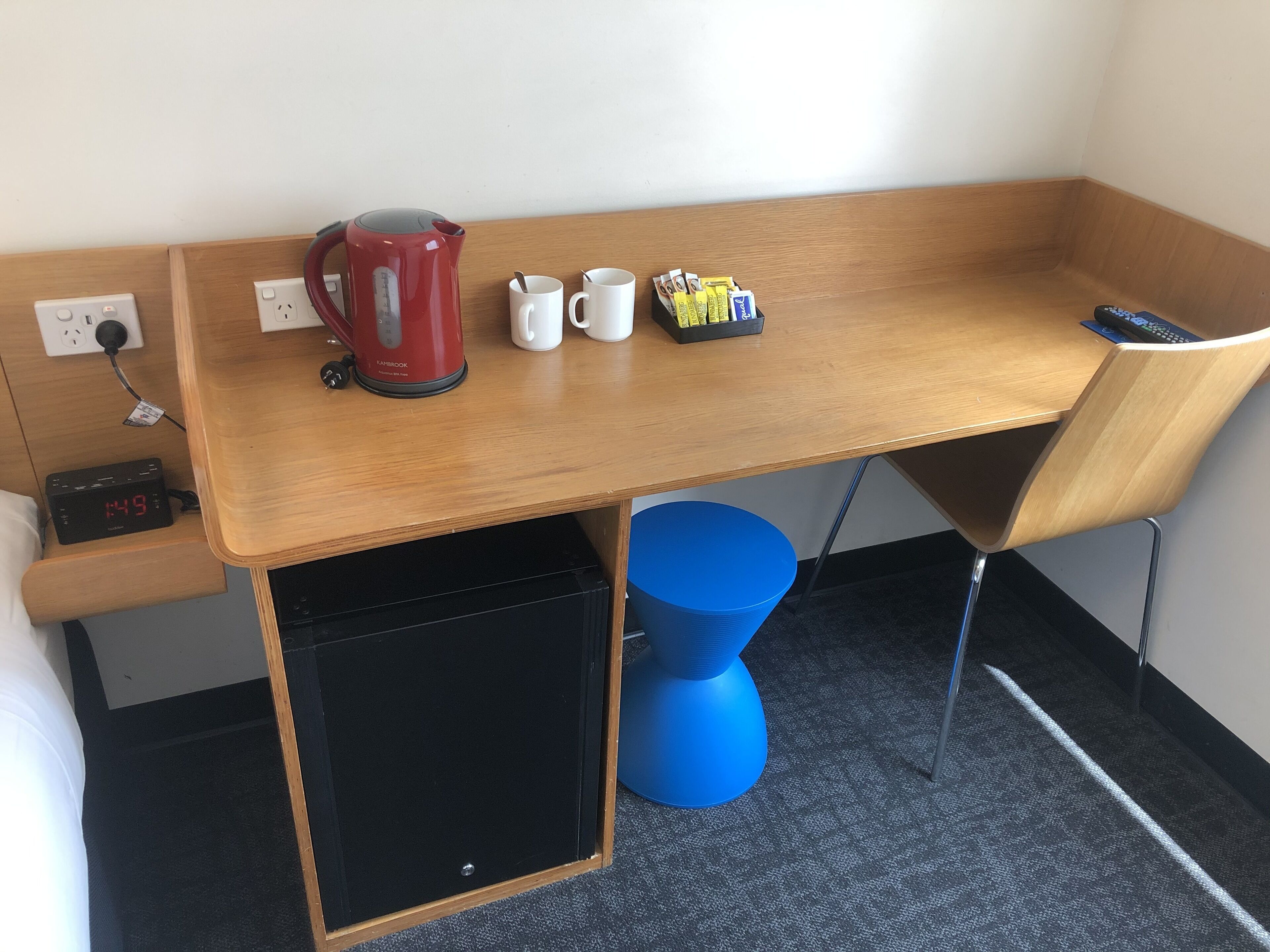 Een houten bureau met een rode waterkoker, twee witte mokken en een schaal met lekkernijen.