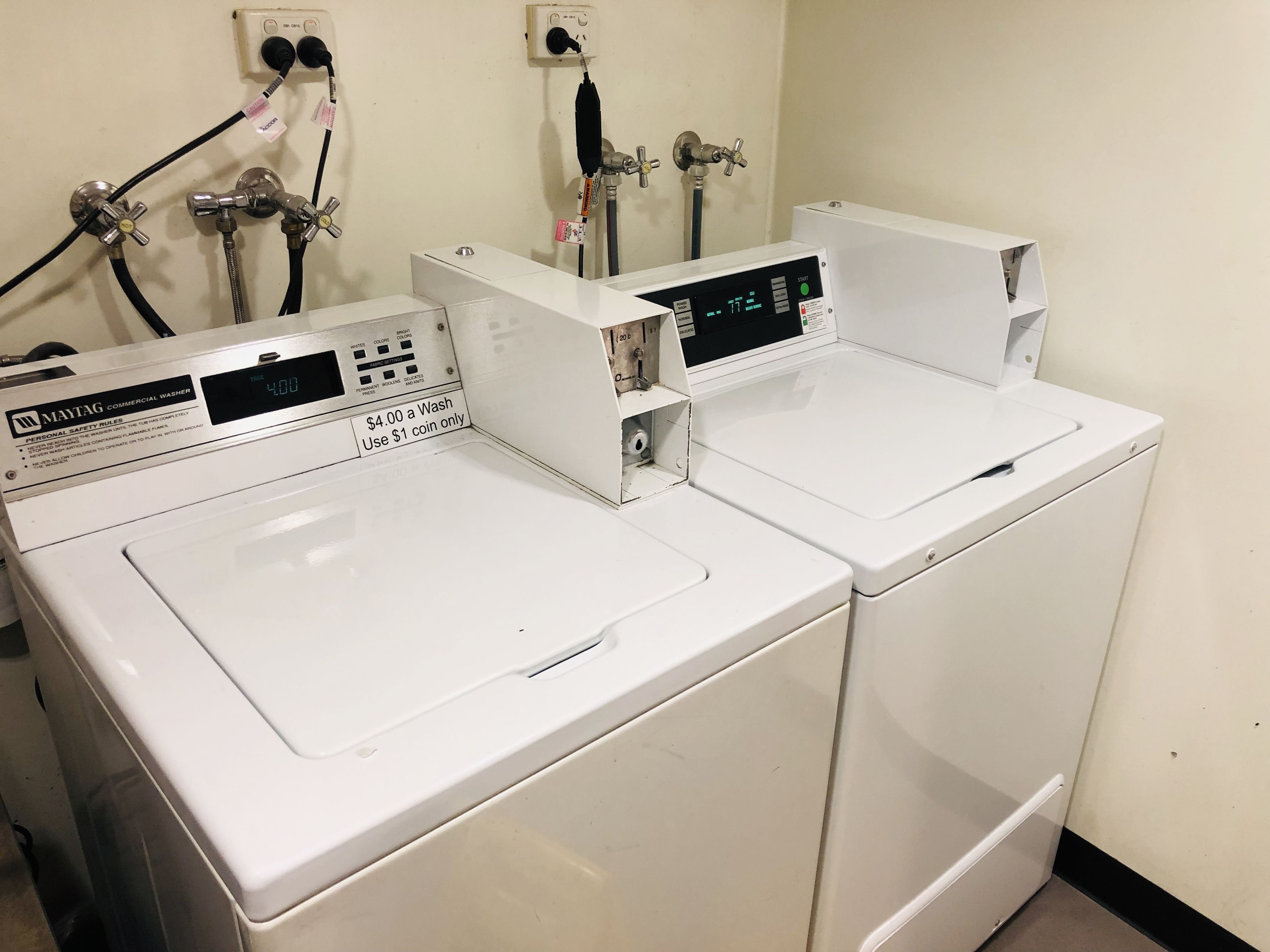Two Maytag commercial washers in a utility room with visible safety rules and a price tag of $4.00 per wash using $1 coin.