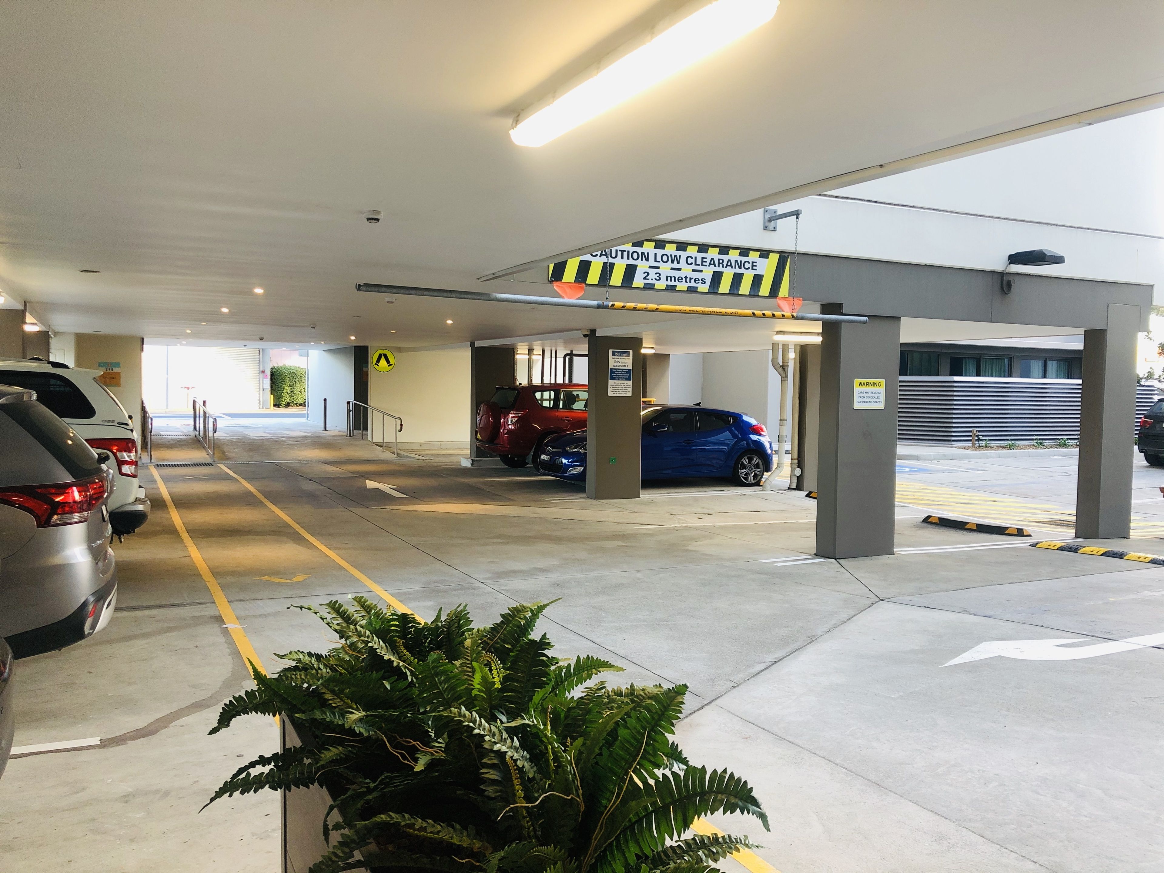 Eine Parkgarage mit mehreren Autos, einem Schild zur Warnung vor geringer Durchfahrtshöhe und Pfeilen auf dem Boden.