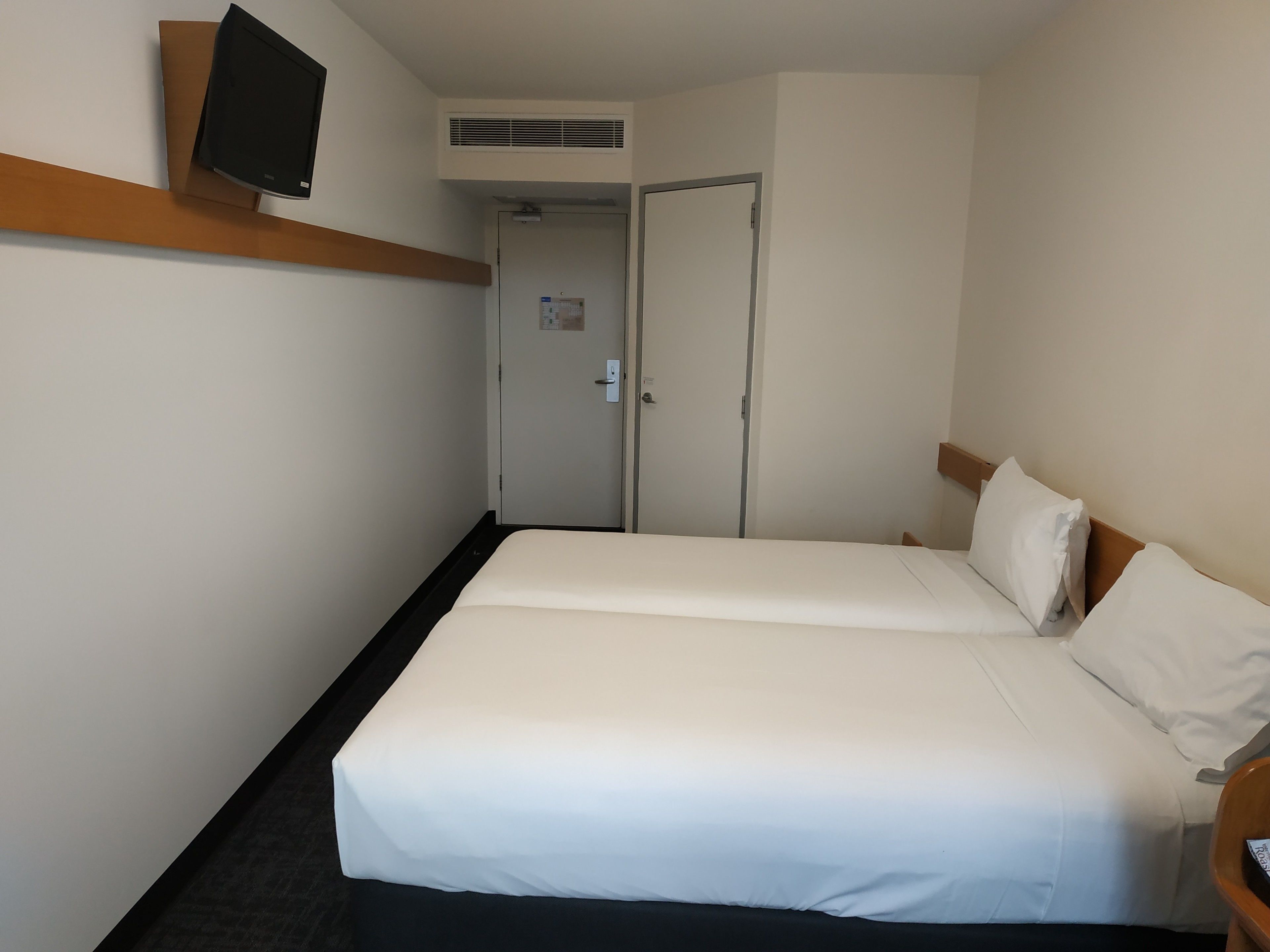 Habitación de hotel con dos camas, un televisor en la pared y una puerta que da a un baño.