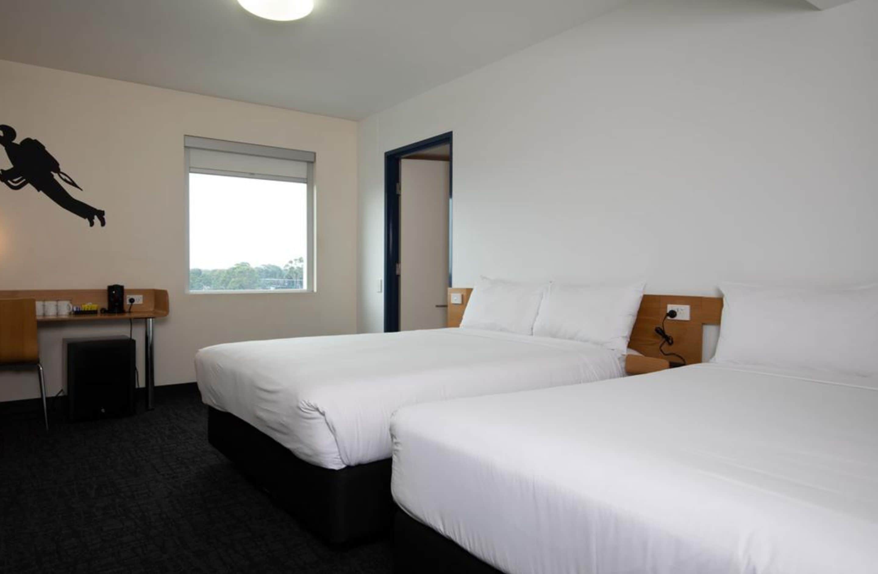 Habitación de hotel con dos camas individuales, un escritorio, una silla y un ventanal con vistas.