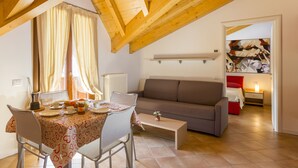 Un coin repas avec une table dressée pour deux personnes, un canapé et un tableau accroché au mur.