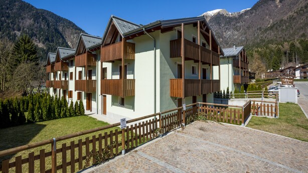 Un immeuble à plusieurs étages doté de balcons, entouré d’une clôture en bois et bordé d’un chemin pavé.