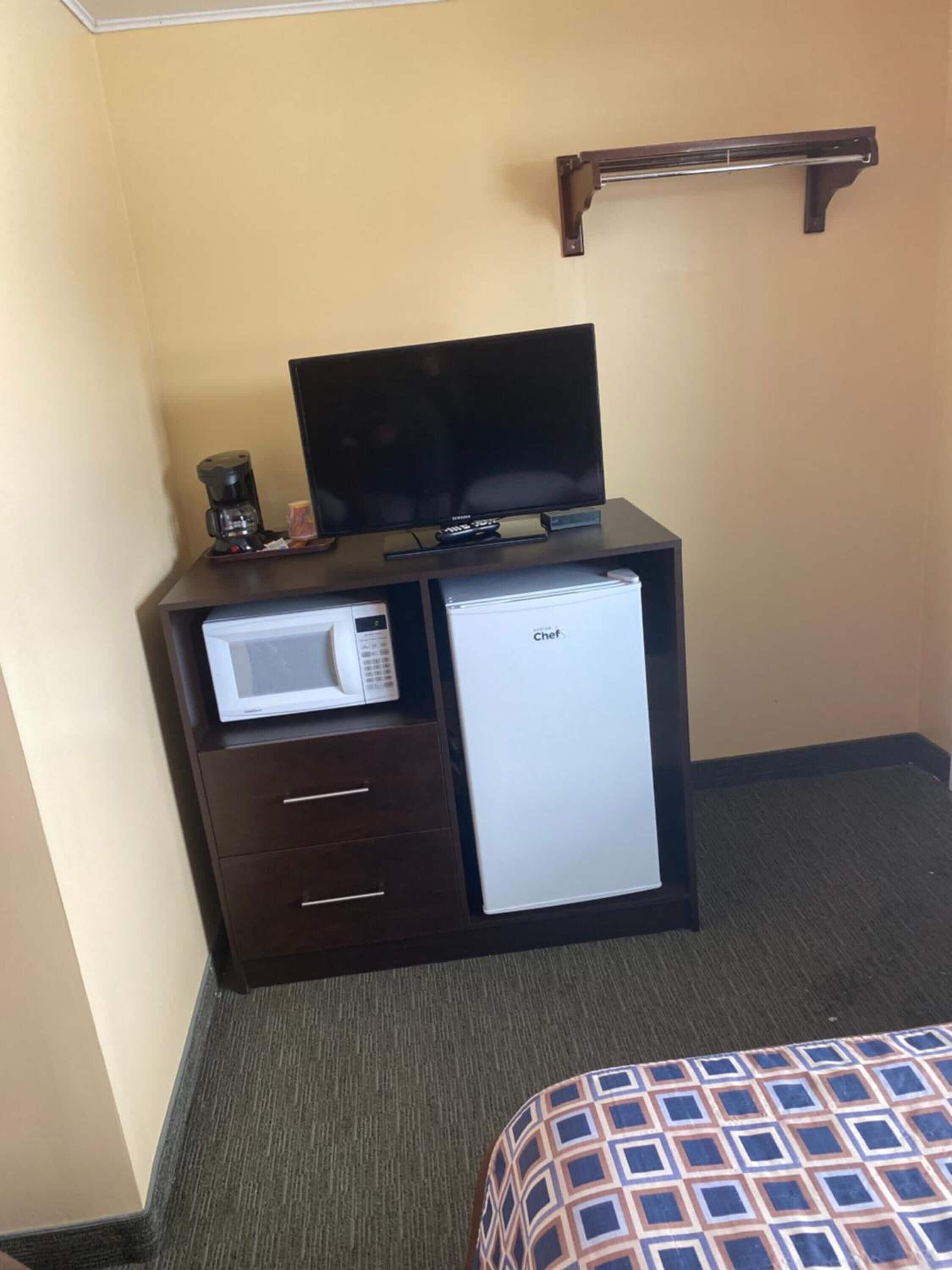 Habitación de hotel con un escritorio de madera oscura, un televisor de pantalla plana, microondas, refrigerador miniatura y una cama con colcha estampada.
